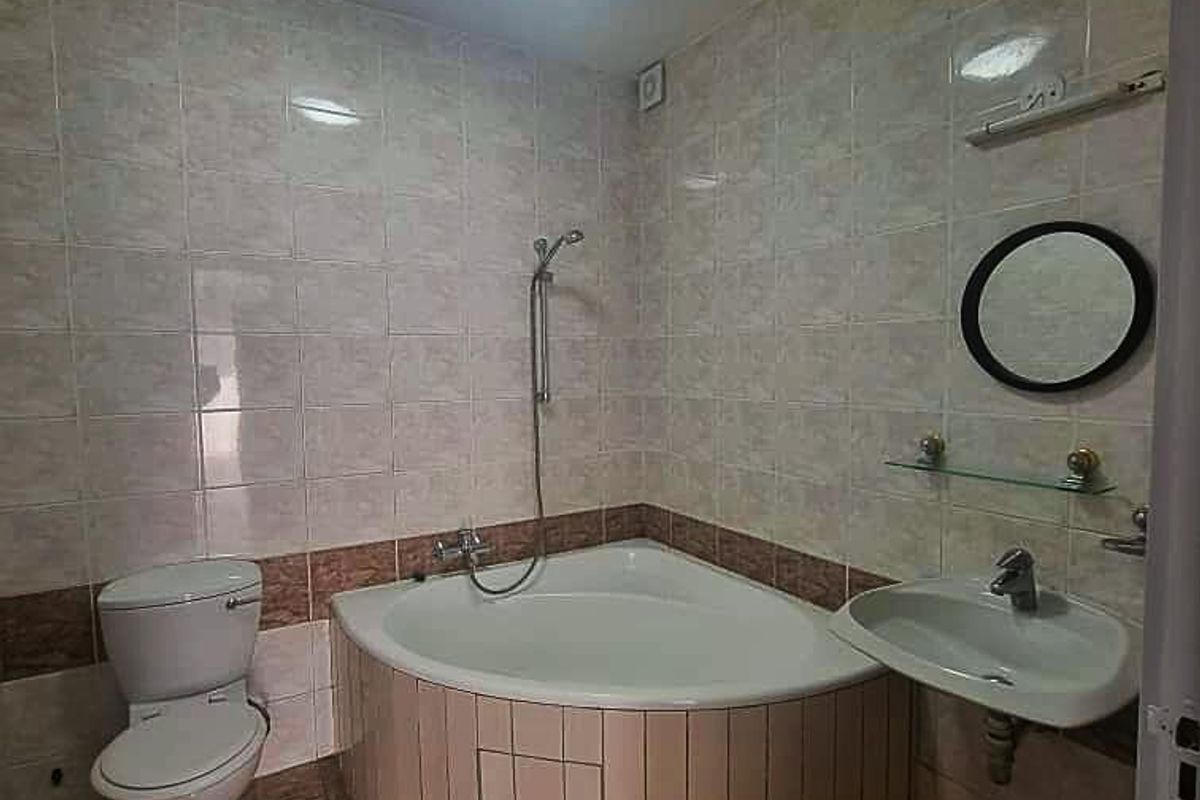 A functional bathroom featuring a corner bathtub, wall-mounted basin, and toilet with neutral tiled finishes throughout.