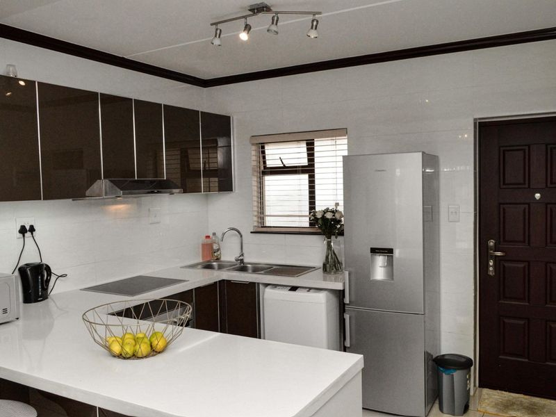 Modern kitchen featuring high-gloss cabinetry, quartz countertops, integrated electric hob, extractor fan, and tiled splashbacks with convenient access to the exterior.
