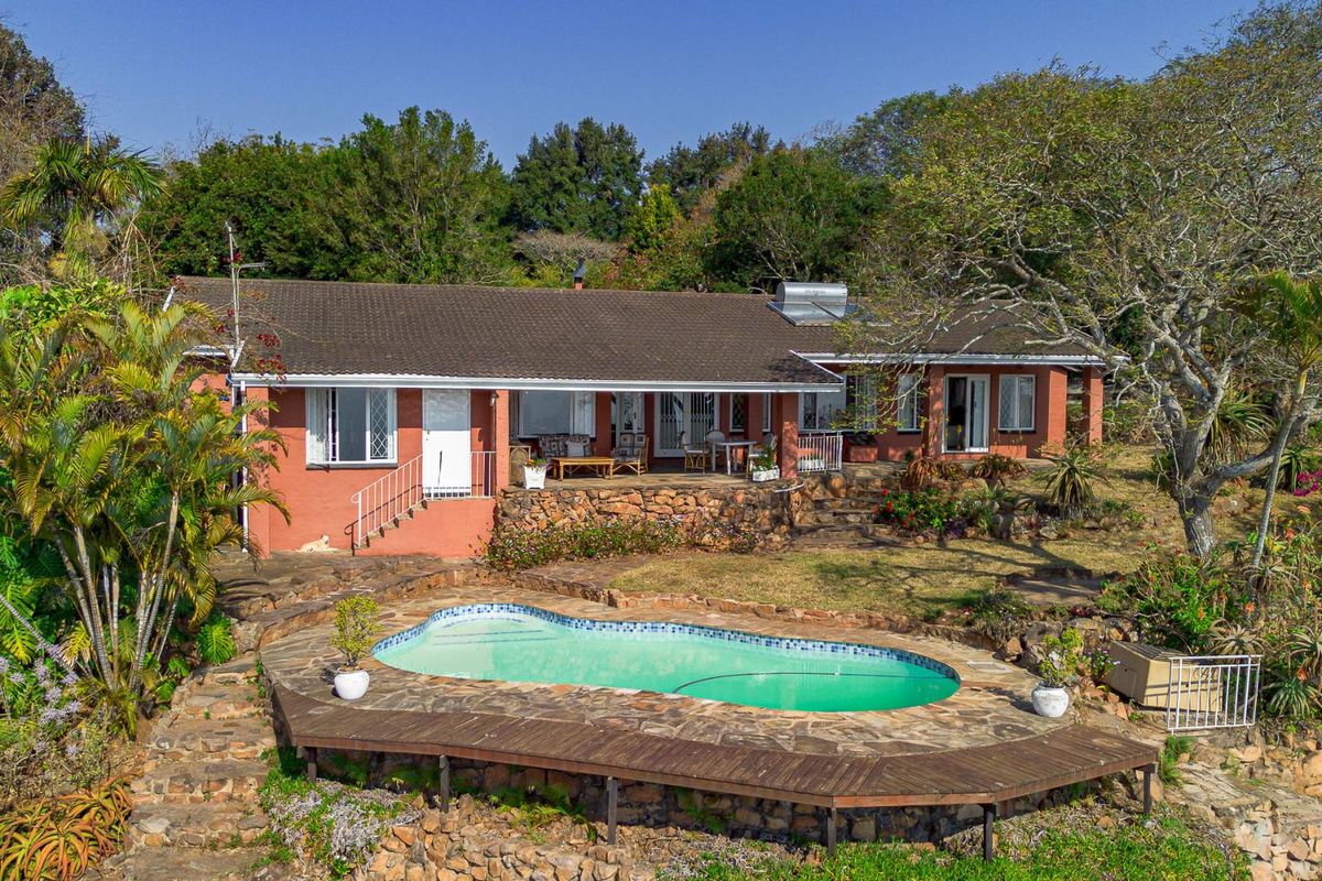 Rear view of the property featuring a swimming pool, stone retaining walls, timber decking, and a covered patio area set within a landscaped garden.