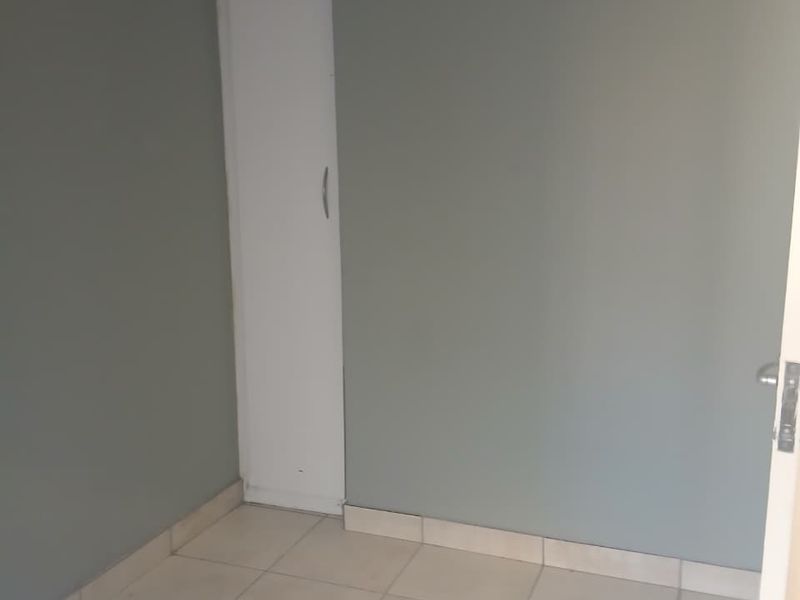 An empty bedroom featuring neutral grey walls, tiled flooring, and a built-in cupboard.