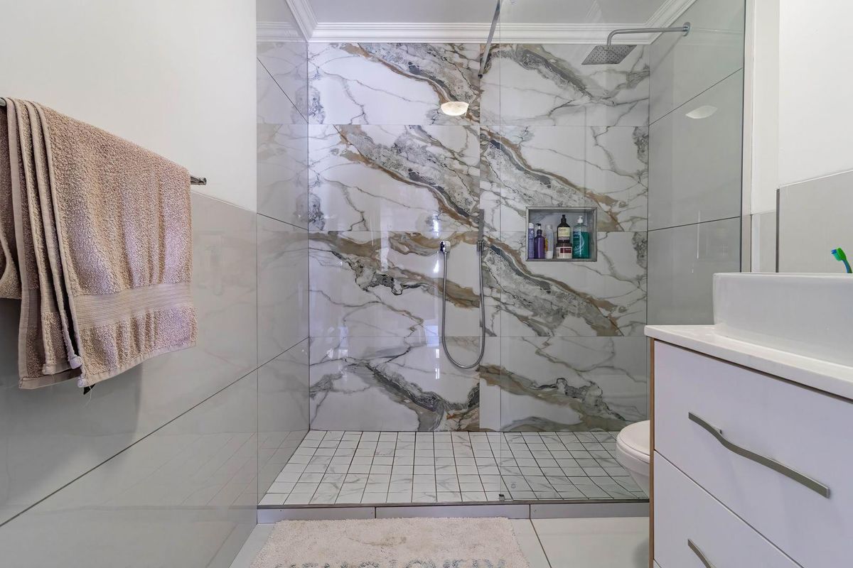 Modern bathroom featuring a walk-in shower with marble-effect wall tiles, a glass shower screen, and a contemporary vanity unit.