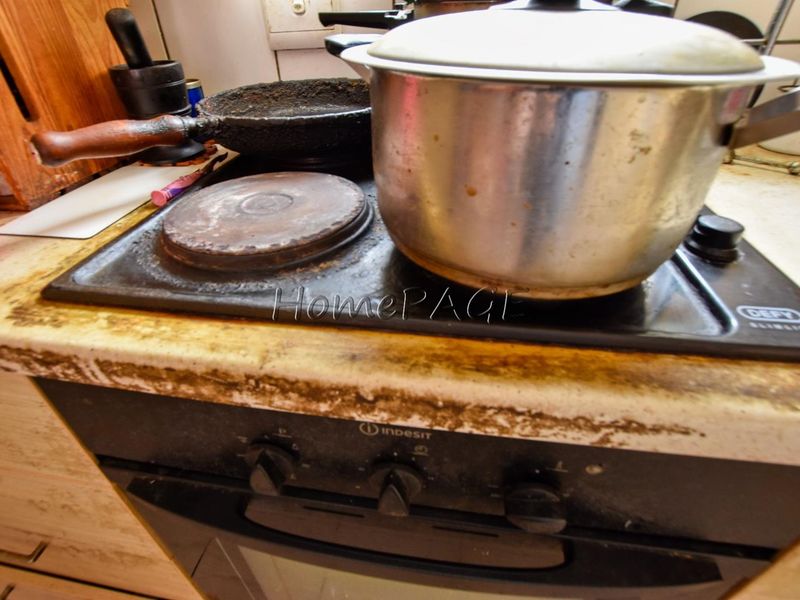 Close-up view of a kitchen cooking area featuring a built-in oven and electric hob with significant wear and surface staining on the countertop.