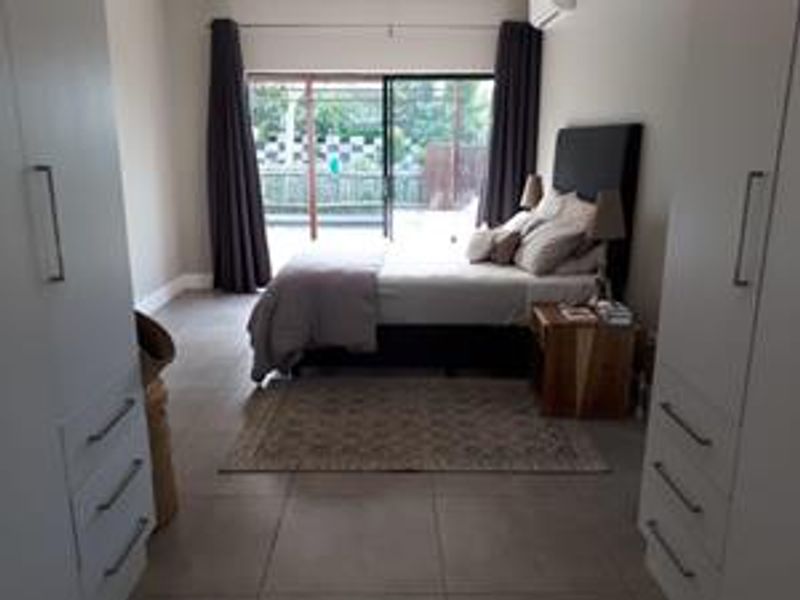 A well-lit bedroom featuring built-in cupboards, tiled flooring, and a sliding glass door providing access to the outdoor area.