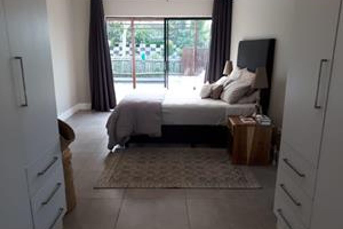 A well-lit bedroom featuring built-in cupboards, tiled flooring, and a sliding glass door providing access to the outdoor area.