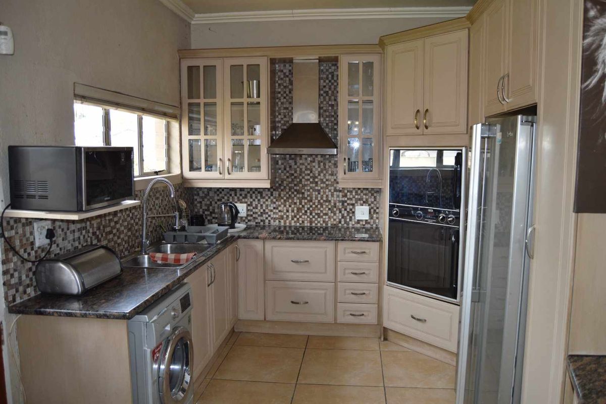 A functional kitchen featuring cream-toned cabinetry, granite countertops, a mosaic tile backsplash, built-in oven, and stainless steel extractor fan.