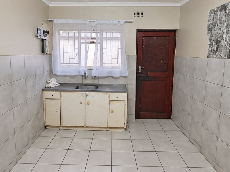 A functional scullery area featuring tiled walls and flooring, a stainless steel sink, and built-in cabinetry, providing a practical space for utility and prep work.