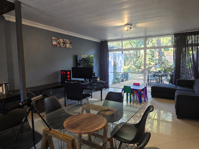 Spacious open-plan living area featuring tiled floors, large sliding glass doors leading to the garden, and a staircase, offering a versatile layout.