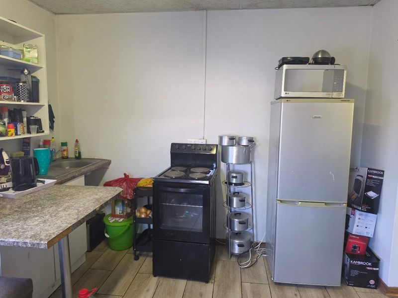 A functional kitchen area featuring a freestanding stove, laminate countertops, a built-in sink, and tiled flooring, offering potential for modernization.