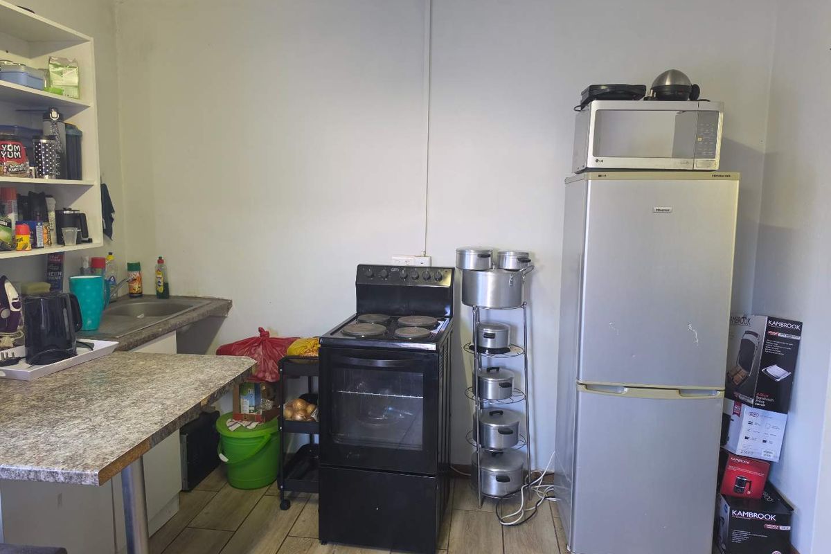 A functional kitchen area featuring a freestanding stove, laminate countertops, a built-in sink, and tiled flooring, offering potential for modernization.
