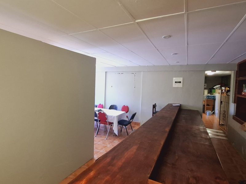 A functional bar area featuring a large built-in wooden counter, tiled flooring, and a suspended ceiling, suitable for hospitality or entertainment use.