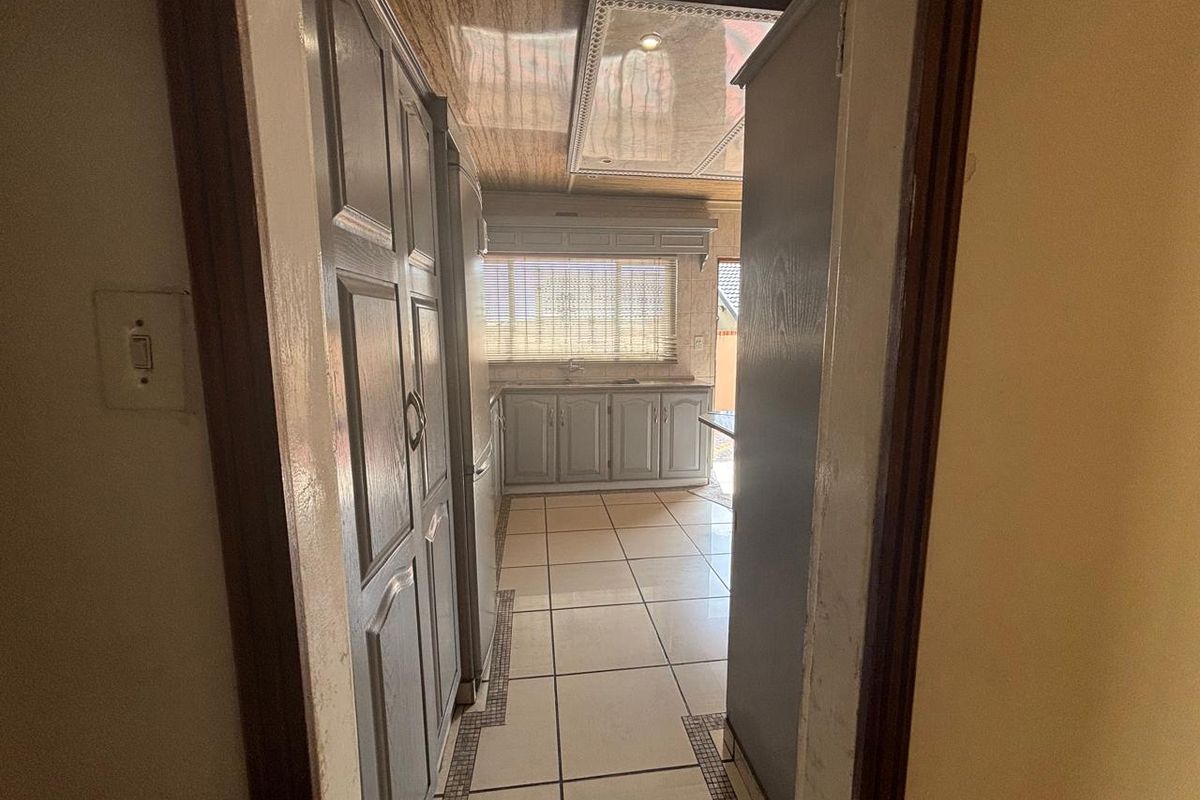 A functional kitchen featuring built-in cabinetry, tiled flooring, and a unique panelled ceiling, providing a practical workspace with direct access to the exterior.