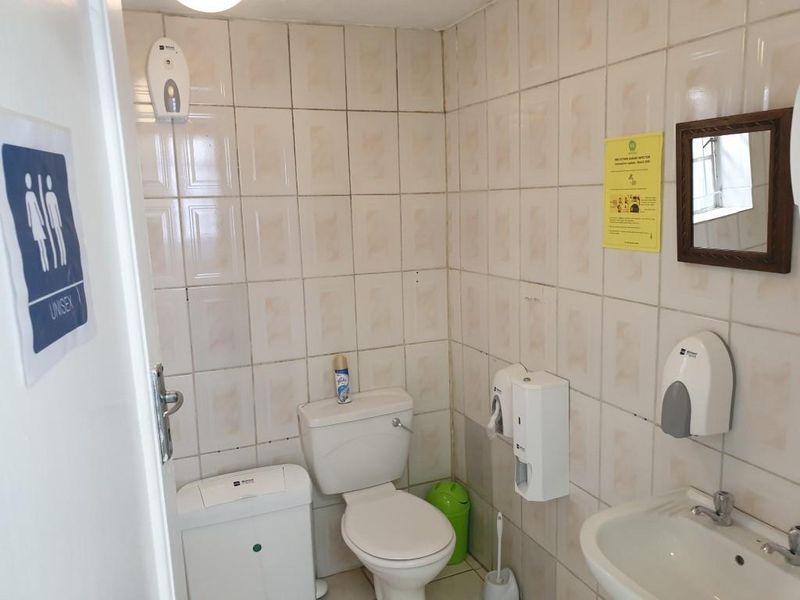 A functional unisex office restroom featuring tiled walls, a standard toilet, and a pedestal washbasin with wall-mounted dispensers.
