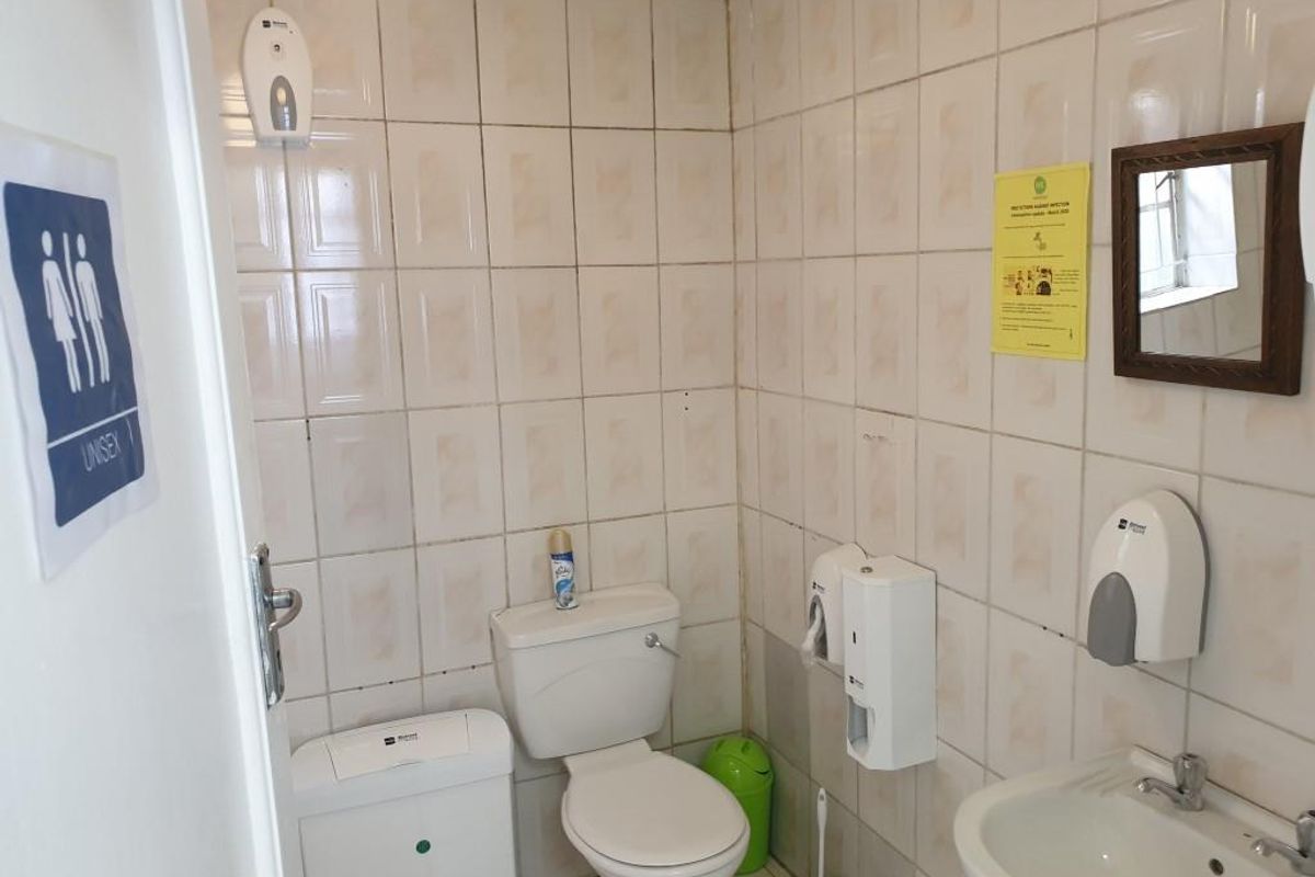 A functional unisex office restroom featuring tiled walls, a standard toilet, and a pedestal washbasin with wall-mounted dispensers.