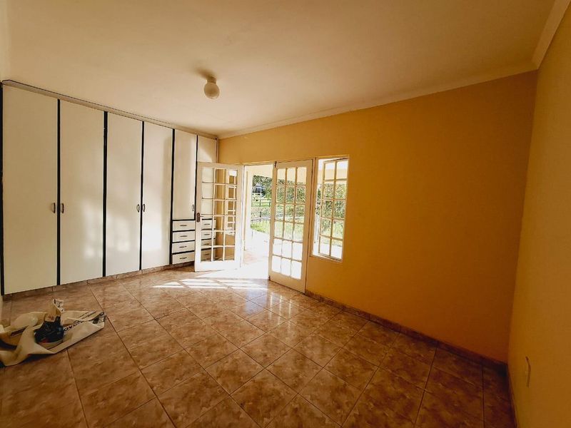 Spacious bedroom featuring built-in cupboards, tiled flooring, and direct access to the garden through classic french doors.