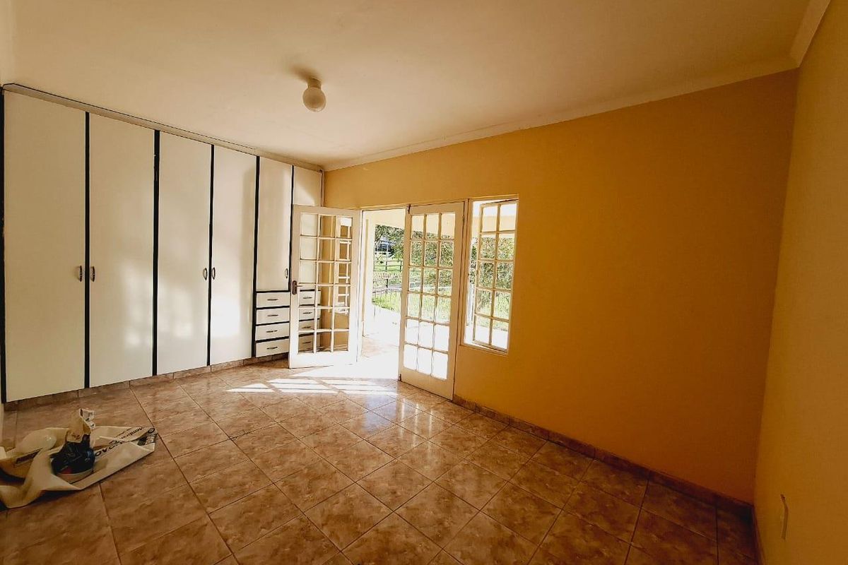 Spacious bedroom featuring built-in cupboards, tiled flooring, and direct access to the garden through classic french doors.