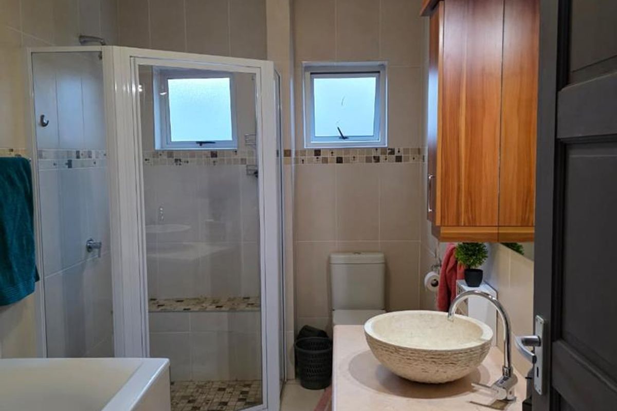 A functional bathroom featuring a corner shower enclosure, a bathtub, a stone vessel sink on a vanity, and neutral wall tiling.