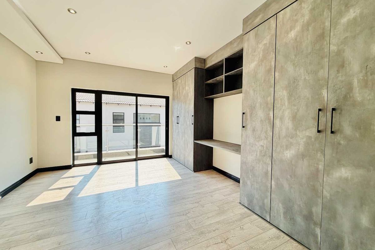 Modern bedroom featuring high-quality built-in cupboards with an integrated desk, laminate flooring, and a sliding glass door leading to an outdoor balcony.