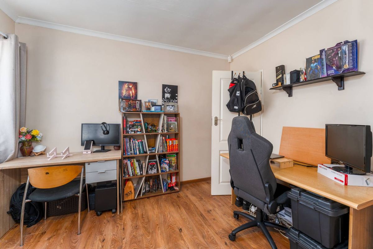 A functional bedroom or home office space featuring wood-look laminate flooring and neutral wall finishes.