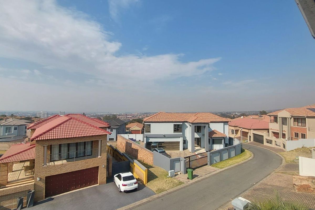An elevated aerial view of a residential neighbourhood featuring multiple detached houses with tiled roofs, paved driveways, and boundary walls.