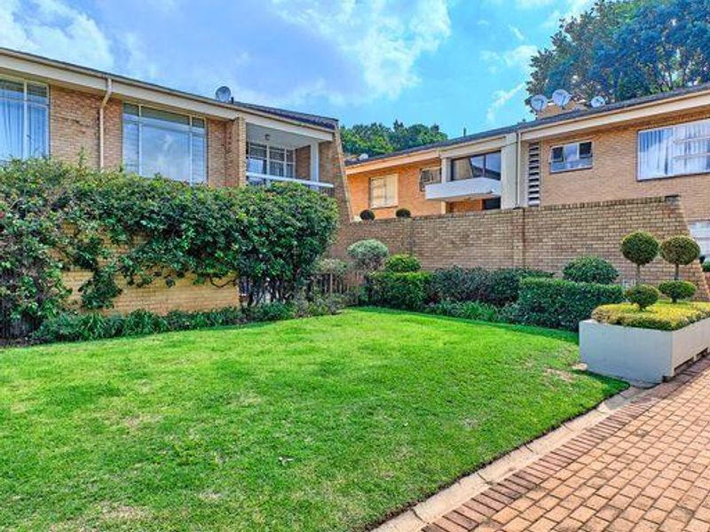 A well-maintained rear exterior view of an apartment complex featuring a lush green lawn, brick facade, and paved walkway.