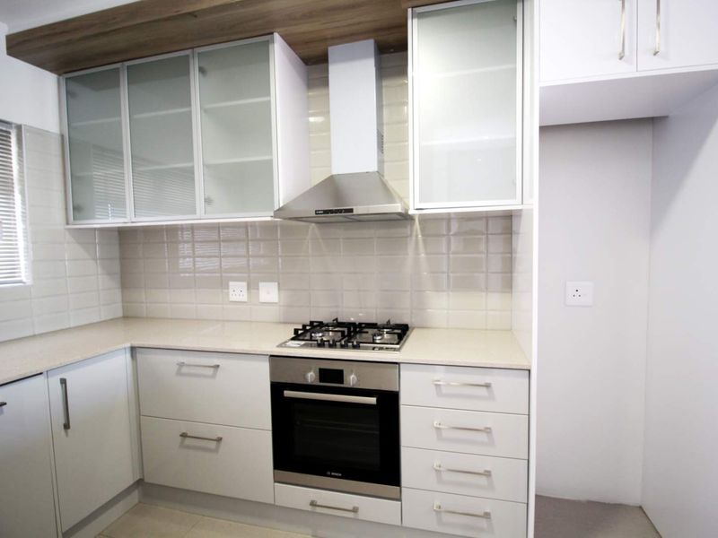 Modern kitchen featuring white cabinetry, stone countertops, a gas hob, built-in oven, extractor fan, and a tiled backsplash.