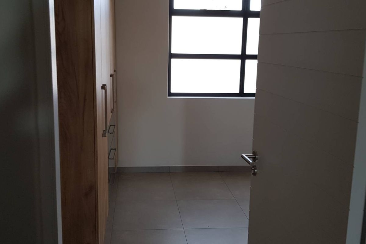 A clean, empty bedroom featuring modern tiled flooring and built-in wooden cupboards, illuminated by a large window.