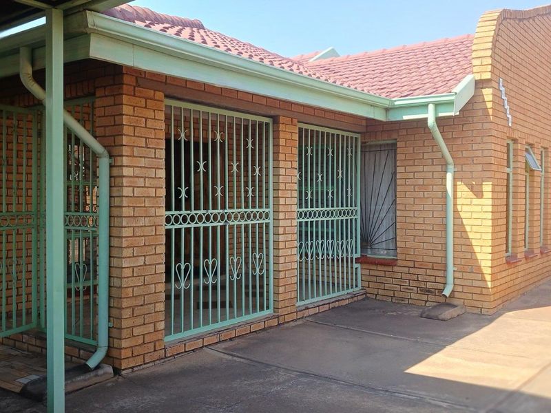 A rear exterior view of a face brick house featuring a tiled roof, concrete patio area, and fitted security gates and bars on windows.