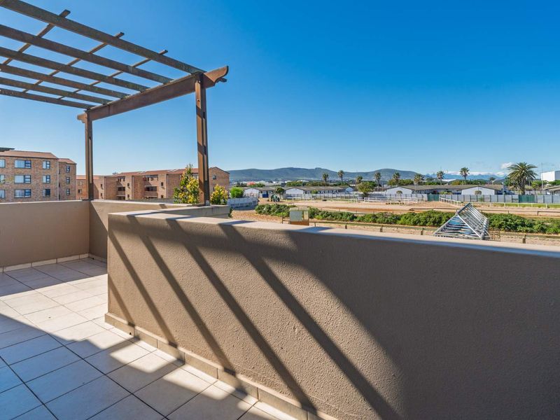 A spacious balcony featuring tiled flooring, a timber pergola, and a masonry balustrade, offering expansive views of the surrounding area.