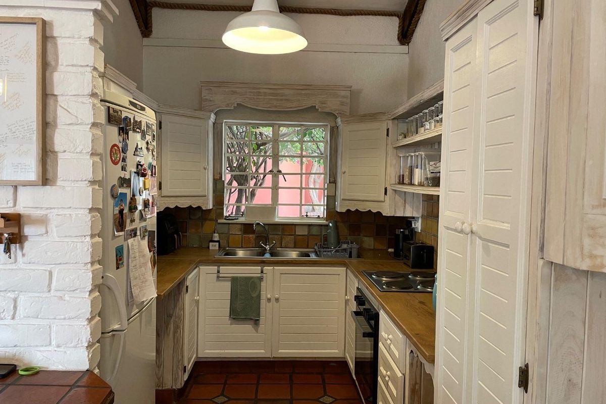 A compact kitchen featuring white cabinetry, wooden countertops, a double sink, and a tiled backsplash with a window overlooking the exterior.