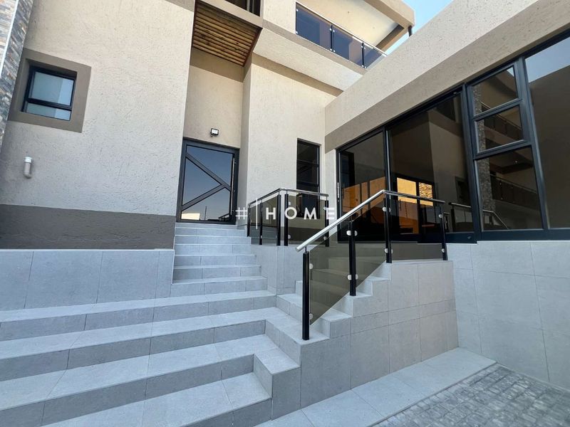 Modern exterior entrance featuring a tiled staircase with glass balustrades and contemporary aluminium framed doors and windows.