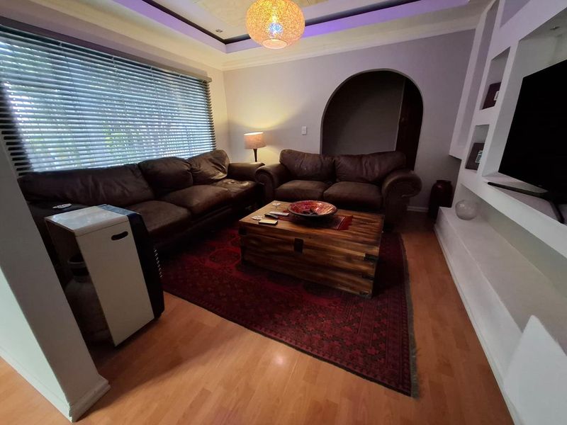 A cozy living room featuring laminate flooring, a recessed ceiling with ambient lighting, an arched doorway, and built-in shelving units.