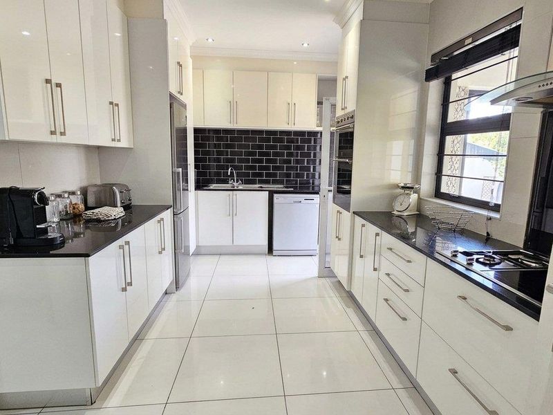 Modern galley-style kitchen featuring high-gloss white cabinetry, contrasting black granite countertops, subway tile backsplash, and integrated stainless steel appliances.