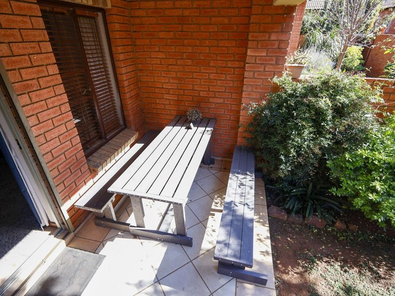 A covered patio area featuring exposed brick walls and tiled flooring, providing direct access to the garden through a sliding glass door.