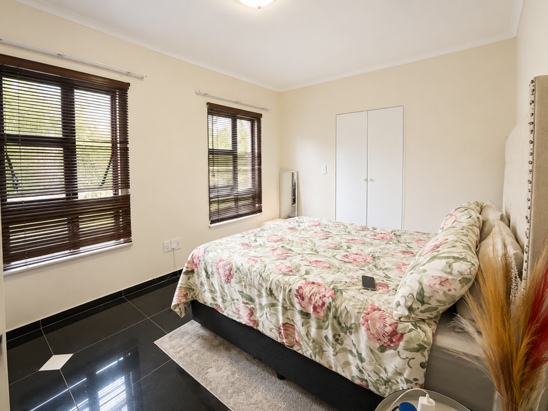 A well-lit bedroom featuring dark tiled flooring, built-in cupboards, and venetian blinds on the windows.