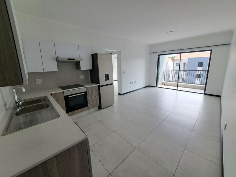 Modern open-plan kitchen and living area featuring tiled floors, built-in cabinetry, integrated appliances, and a sliding door leading to a private balcony.
