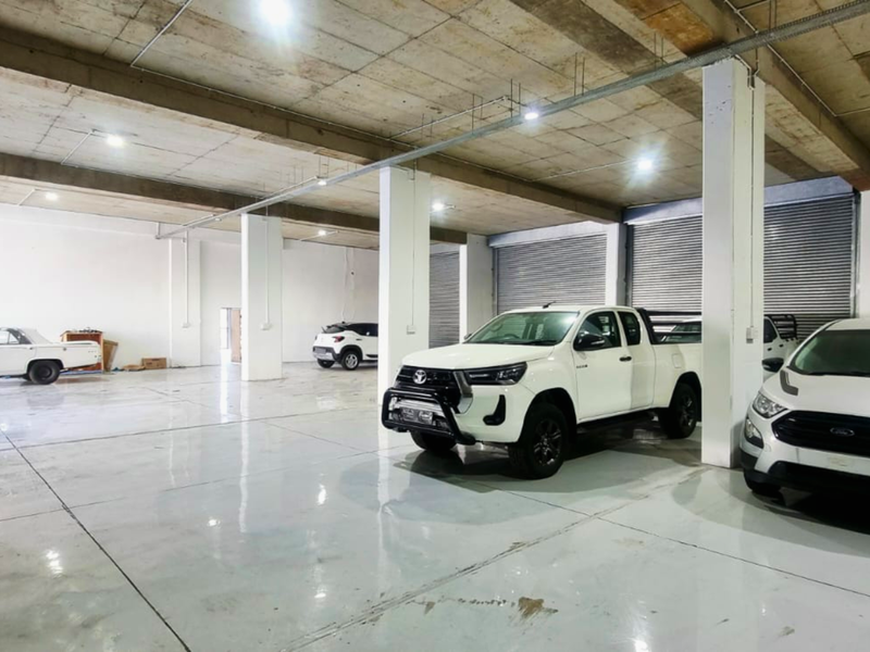 Spacious industrial garage featuring high exposed concrete ceilings, durable epoxy flooring, and multiple roller shutter doors for easy vehicle access.