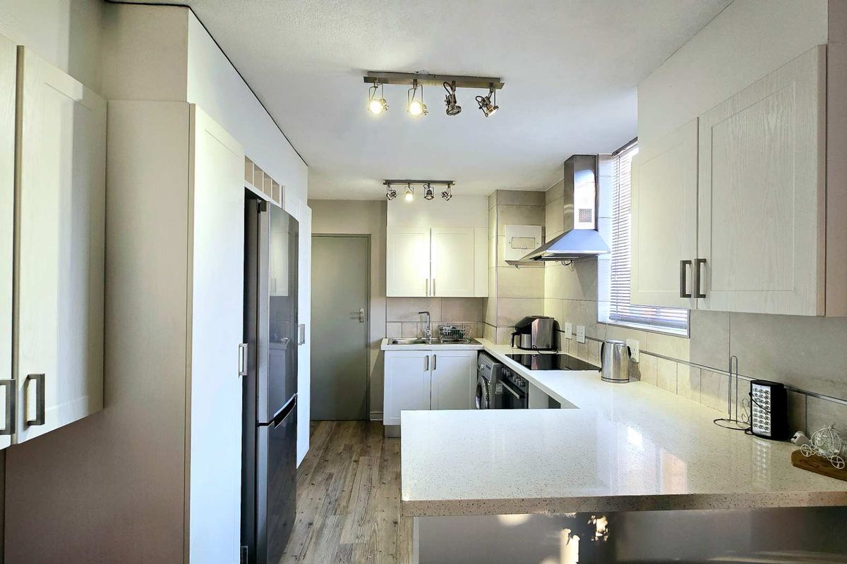A modern kitchen featuring white cabinetry, stone countertops, a stainless steel extractor fan, and wood-look flooring.