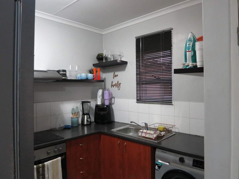 Compact scullery featuring built-in cabinetry, stainless steel sink, electric oven, hob, and extractor fan with tiled splashback and venetian blinds.