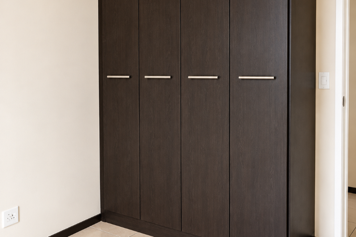 A clean, empty bedroom featuring a modern dark wood built-in wardrobe and neutral tiled flooring.