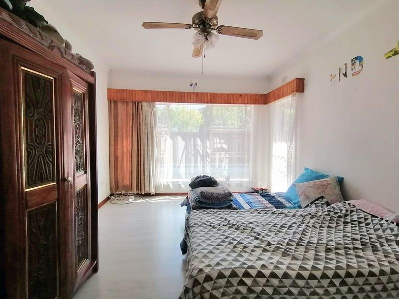A bedroom featuring a ceiling fan, wooden pelmet detailing, and a large window allowing natural light into the space.