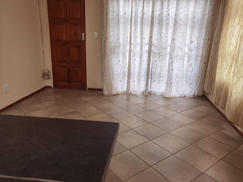 An empty living area featuring neutral tiled flooring and a wooden door, with access to a patio through a sliding glass door.