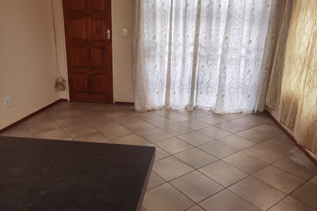 An empty living area featuring neutral tiled flooring and a wooden door, with access to a patio through a sliding glass door.
