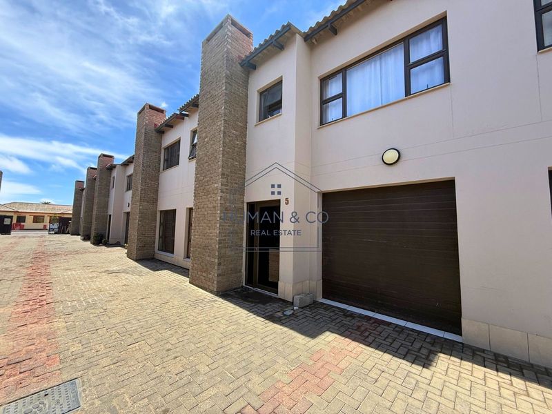 Front elevation of a townhouse featuring a paved driveway, integrated garage, and distinctive brick chimney stacks.