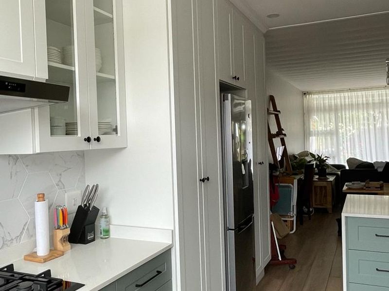 Modern open-plan kitchen featuring shaker-style cabinetry, quartz countertops, integrated appliances, and wood-look tile flooring, flowing into the adjacent living area.