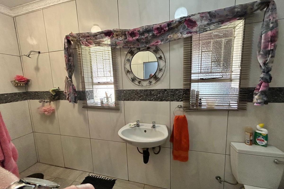 A functional bathroom featuring wall-mounted basin, toilet, and shower area with tiled walls and decorative mosaic border.