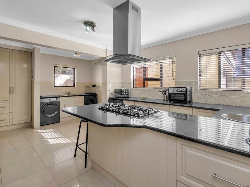 A well-appointed kitchen featuring a central island with a gas hob, granite countertops, ample built-in cabinetry, and a tiled backsplash.