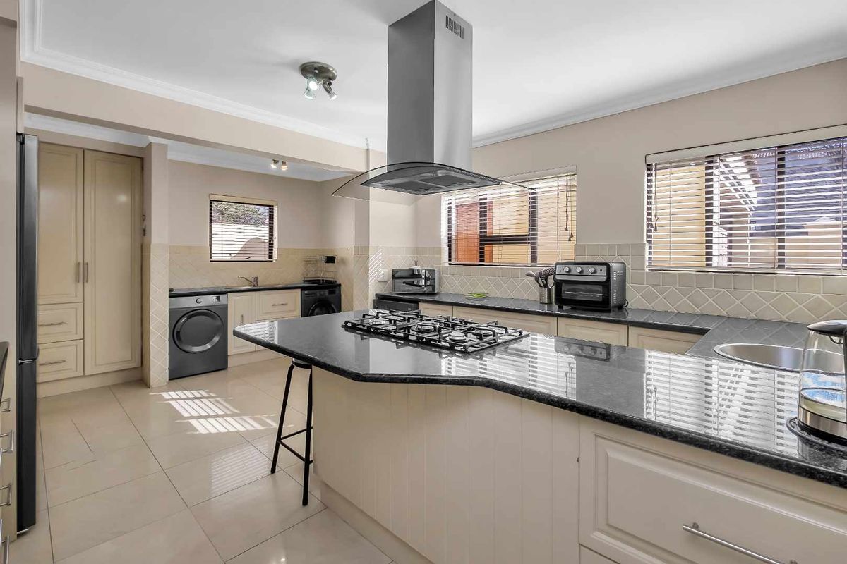 A well-appointed kitchen featuring a central island with a gas hob, granite countertops, ample built-in cabinetry, and a tiled backsplash.