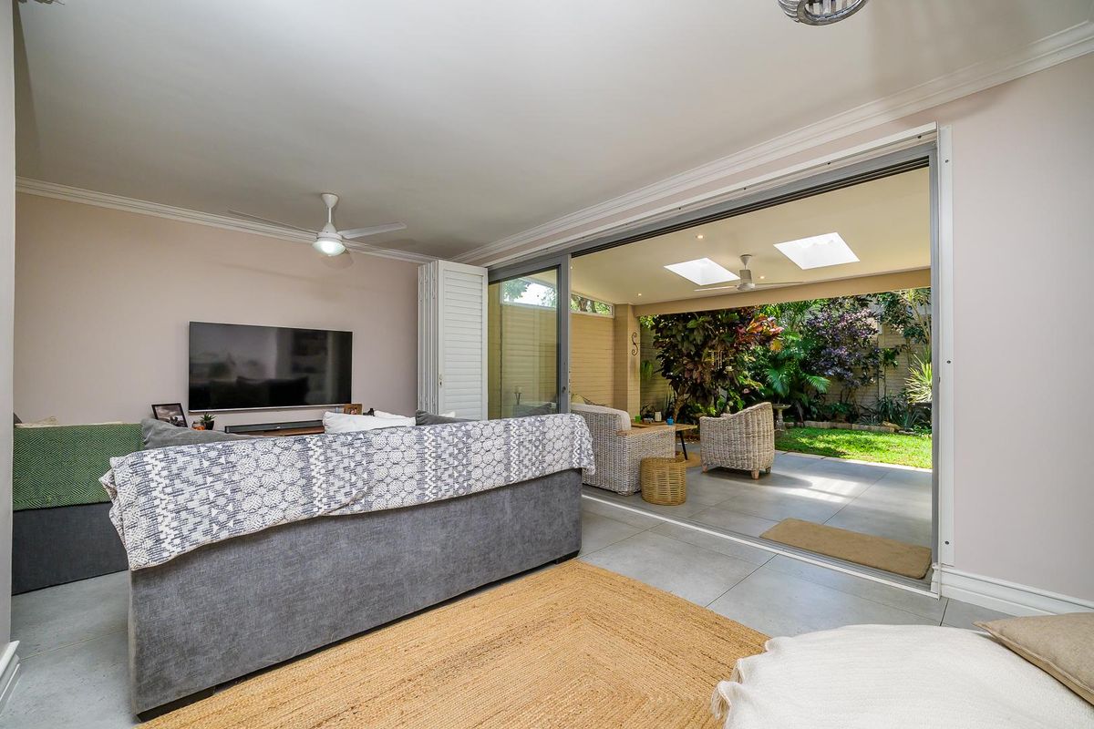 A bright living room featuring large sliding glass doors that open onto a covered patio and landscaped garden area.