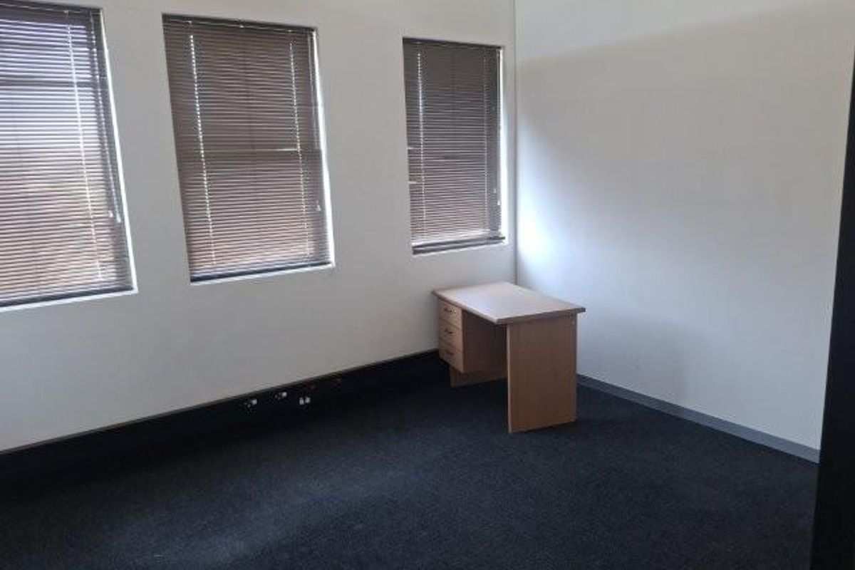 A vacant office space featuring neutral walls, dark carpeting, and multiple windows fitted with venetian blinds.
