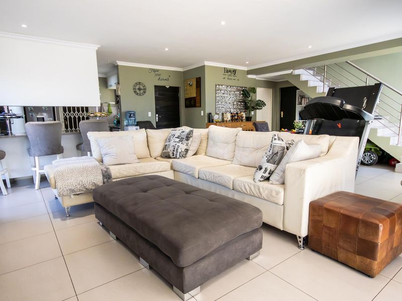 Spacious open-plan living area featuring tiled floors, recessed lighting, and a staircase, seamlessly connecting to the kitchen and breakfast bar area.